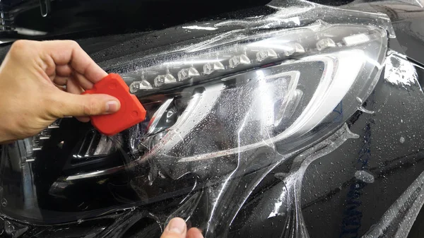 Ön far ve kaputta Ppf montaj işlemine yakın. Ppf, boyayı çizilmelerden ve taş yongalarından koruyan bir Boya Koruma Filmidir. Konsept: Koruma, Koruma, Araba, Yeni, İş.