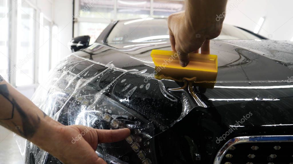 Close up to PPF installation process on a front headlight and hood. PPF is a Paint Protection Film which protect paint from scratches and stone chips. Concept of: Guard, Protect, Car, New, Work.