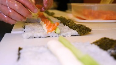 Profesyonel şefin elleri şeffaf eldivenlerle bir restoranda suşi yaparken ve rulo yaparken. Geleneksel Japon yemekleri. Hazırlık süreci. Hazırlama, Yuvarlama, Salamon.