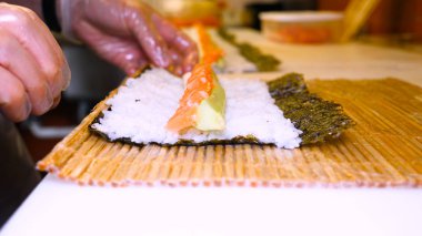 Profesyonel şefin elleri şeffaf eldivenlerle bir restoranda suşi yaparken ve rulo yaparken. Geleneksel Japon yemekleri. Hazırlık süreci. Hazırlama, Yuvarlama, Salamon.