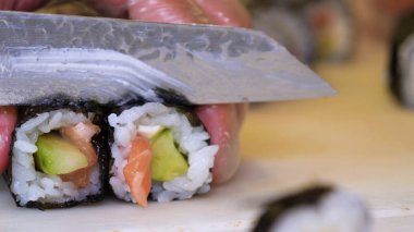 Profesyonel şefin elleri şeffaf eldivenlerle bir restoranda suşi yaparken ve rulo yaparken. Geleneksel Japon yemekleri. Hazırlık süreci. Hazırlama, Yuvarlama, Salamon.