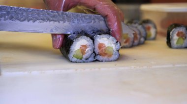 Profesyonel şefin elleri şeffaf eldivenlerle bir restoranda suşi yaparken ve rulo yaparken. Geleneksel Japon yemekleri. Hazırlık süreci. Hazırlama, Yuvarlama, Salamon.