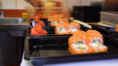 Profesyonel şefin elleri şeffaf eldivenlerle bir restoranda suşi yaparken ve rulo yaparken. Geleneksel Japon yemekleri. Hazırlık süreci. Hazırlama, Yuvarlama, Salamon.