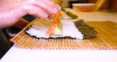Profesyonel şefin elleri şeffaf eldivenlerle bir restoranda suşi yaparken ve rulo yaparken. Geleneksel Japon yemekleri. Hazırlık süreci. Hazırlama, Yuvarlama, Salamon.