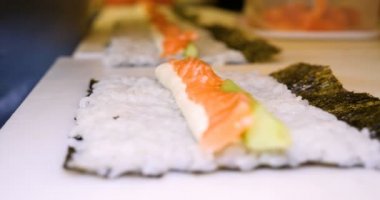 Profesyonel şefin elleri şeffaf eldivenlerle bir restoranda suşi yaparken ve rulo yaparken. Geleneksel Japon yemekleri. Hazırlık süreci. Hazırlama, Yuvarlama, Salamon.