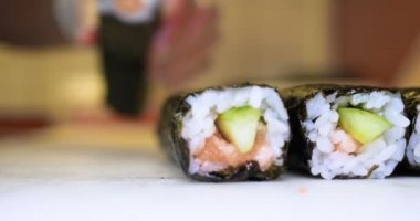 Profesyonel şefin elleri şeffaf eldivenlerle bir restoranda suşi yaparken ve rulo yaparken. Geleneksel Japon yemekleri. Hazırlık süreci. Hazırlama, Yuvarlama, Salamon.