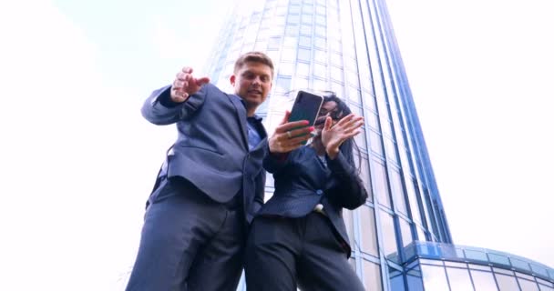 超高層ビルを背景に携帯電話でセルフィーを撮る楽しいカップル コンセプト スイート ビジネス カップル スマートフォン ライフスタイル 5Gネットワーク — ストック動画