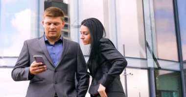 Gökdelen arka planında cep telefonuyla selfie çeken eğlenceli genç çift. Süit, İş, Çift, Mimarlık, Akıllı Telefon, Yaşam Tarzı, 5G Ağı.