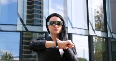 Takım elbiseli genç güzel iş kadını (öğrenci) portresi, gelecek gözlükleri, güler yüzlü, başarılı yanlara bakan, gökdelen arka planlı. Konsept: Yeni iş, İletişim, Gelecek, Yönetici.