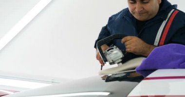 İşçi araba cilasıyla araba cilalıyor. Çalışanların ellerini oto cilalayıcı kullanarak atölyedeki araba gövdesini parlatmak için kapatın.