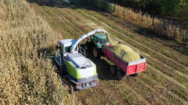 Aerial shot of harvester loading off corn on trailers. Aerial shot of modern harvester loading off corn on tractor trailers. Concept of: Tractor, Harvest, Drone, Eco.