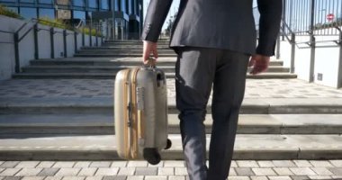 Seyahat eden işadamı tekerlekli bavuluyla şehrin silüetini geçiyor, iş adamı bavuluyla yürüyor ve cep telefonu kullanıyor..