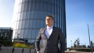 Başarıyı kutluyoruz. Heyecanlı genç işadamının kollarını havada tutması ve arka planda ofis binasıyla dışarıda durarak pozitifliğini ifade etmesi düşük açılı bir bakış açısı.