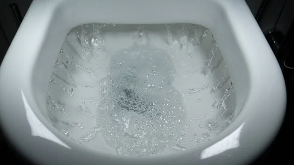 Sifonu çek. Su, sifonu çeker. Suyun akışı açıkça görülebilir. Seramik tuvalette parlayan su.