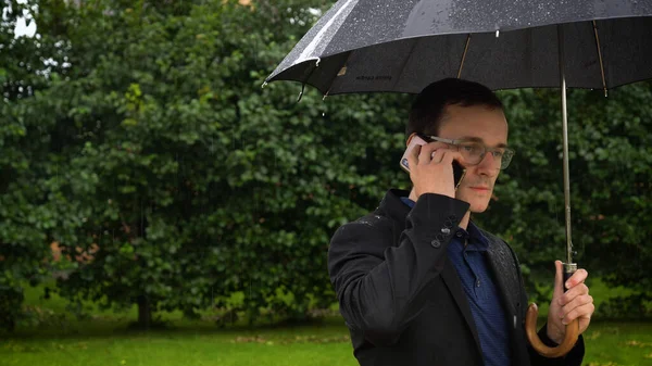 lose up of a businessman holding an umbrella over his head while talking on a mobile phone.