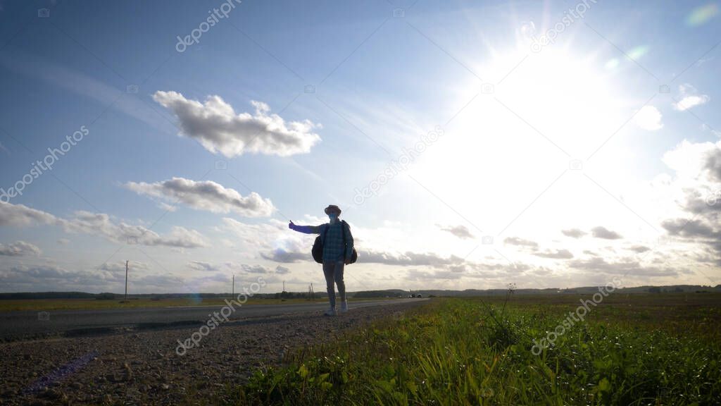A young man is hitchhiking around the country. The man is trying to catch a passing car for traveling. The man with the backpack went hitchhiking to south.