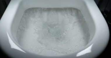 Sifonu çek. Su, sifonu çeker. Suyun akışı açıkça görülebilir. Seramik tuvalette parlayan su.