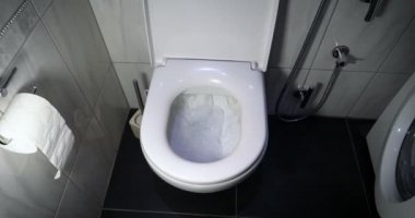 Sifonu çek. Su, sifonu çeker. Suyun akışı açıkça görülebilir. Seramik tuvalette parlayan su.