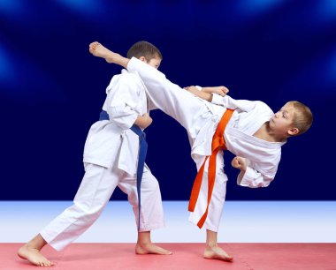 İki sporcu eğitim koyu mavi bir arka plan üzerinde her diğer karşılamak için el ve darbe bacak yumruk