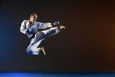 Mavi bindirmeleri elleri olan bir adam bir sıçrama bir tekme atıyor