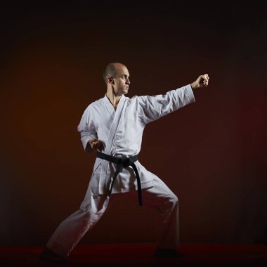 Siyah kuşak sporcu resmi karate çalışmaları karanlık bir arka plan üzerinde gerçekleştirir.