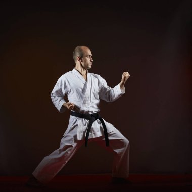 Karanlık bir arka plan üzerinde bir atlet karategi içinde resmi karate çalışmaları gerçekleştirir.