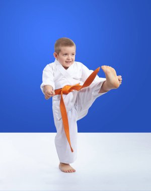 Mavi arka planda Karateka, ileri doğru tekme antrenmanı yapıyor.