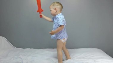 Gri arka planda kırmızı oyuncak kılıçlı iki yaşında bir çocuk.