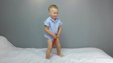 Kırmızı oyuncak bir kılıçla, iki yaşında bir çocuk beyaz bir kapakta oynuyor.