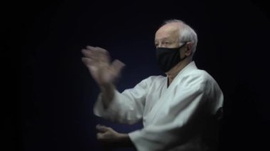 Siyah bir tıbbi maskeyle, yaşlı bir atlet karanlık bir arka plana karşı blok ve yumruklar eğitiyor.