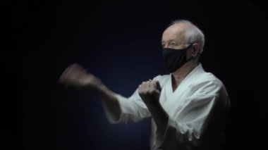 Siyah bir tıbbi maskeyle, yaşlı bir atlet karanlık bir arka plana karşı eğitim blokları oluşturuyor.