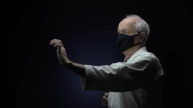 Siyah bir tıbbi maskeyle, yaşlı bir sporcu karanlık bir arka plana yumruk atar.