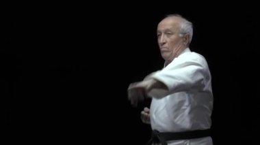 Siyah arka planda yaşlı bir erkek sporcu elleriyle tekme ve blok yapıyor.