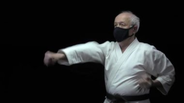 Yaşlı atlet, elleri siyah bir tıbbi maske takmış yumruklar ve bloklar yapıyor.