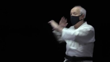 Siyah arka planda, yaşlı bir atlet kendini izole etmek için resmi karate egzersizleri yapıyor.