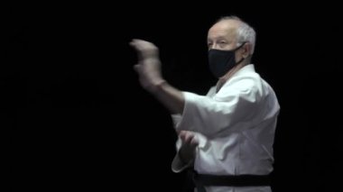 Siyah bir tıbbi maskeyle, yaşlı bir atlet elleri siyah bir arka planda blokları eğitiyor.
