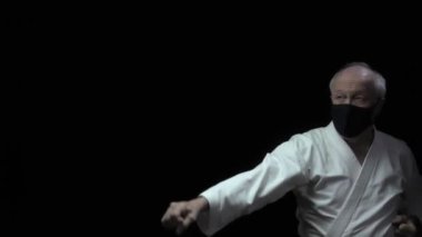 Siyah tıbbi bir maskeyle karate duruşunda, yaşlı bir atlet kolları ve kolları eğitir ve yumruklar.