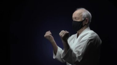 Siyah bir tıbbi maskeyle, yaşlı bir sporcu koyu mavi bir arka plana yumruk atıyor.