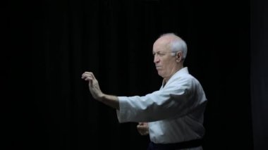 Karategi 'nin siyah arka planında, yaşlı bir atlet el yumrukları eğitiyor.