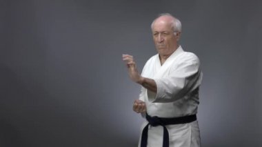 Gri arka planda, yaşlı bir erkek sporcu blokları eğitiyor ve kollarını yumrukluyor.