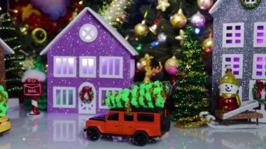 Çatıda Noel ağacı olan turuncu bir araba bir Noel köyünün ortasında duruyor.