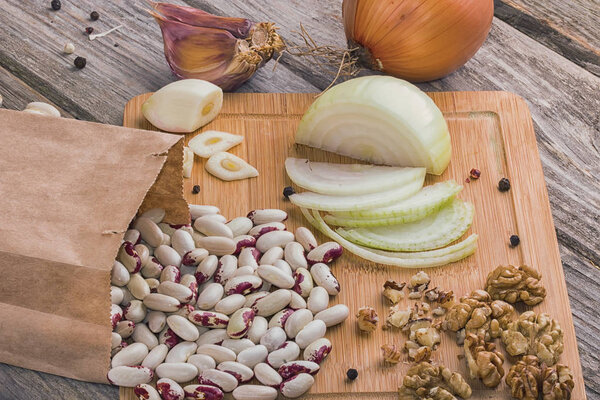 bean seeds in a paper bag, walnut kernel, onion, garlic on a wooden board