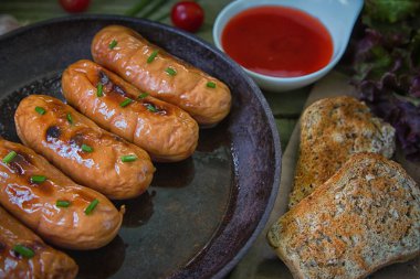 Yeşil soğan, domates sosu, yeşil ot ahşap arka plan üzerinde küçük bir tavada kızarmış sosis. Buğday sağlıklı ekmek dahil tohumları ile.