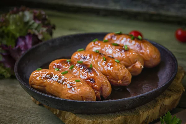 Fried sauseges with green onions, tomato souce, green herb  in a small pan on a wooden  background. Wheat healthy bread with seeds included.