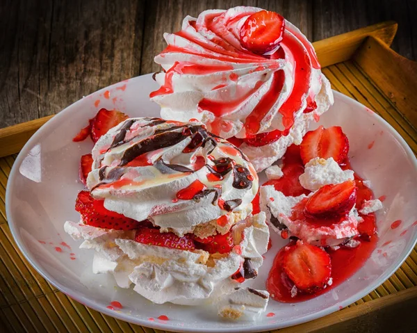 Meringue dessert Pavlova cake with fresh strawberries in white plate on wooden background.