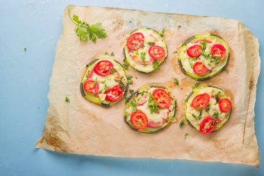 Biber, domates, peynir ve maydanoz parşömen kağıt üzerine açık mavi renkli üzerinde pizza sağlıklı, besleyici kabak küçük yuvarlak.