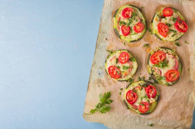 Biber, domates, peynir ve maydanoz parşömen kağıt üzerine açık mavi renkli üzerinde pizza sağlıklı, besleyici kabak küçük yuvarlak.
