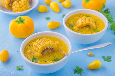 Güzel bir soğuk çorba sarı renk - tatlı Mısır gazpacho, sarı domates ve sarı biber, Mısır ve maydanoz mavi bir arka plan üzerinde beyaz kase bir parçası ile tepesinde. Vejetaryen kavramı.