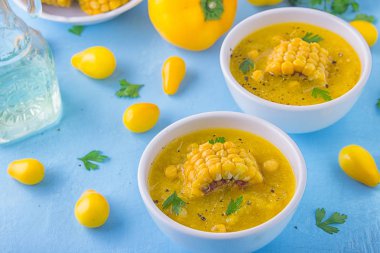 Güzel bir soğuk çorba sarı renk - tatlı Mısır gazpacho, sarı domates ve sarı biber, Mısır ve maydanoz mavi bir arka plan üzerinde beyaz kase bir parçası ile tepesinde. Vejetaryen kavramı.