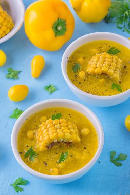 Güzel bir soğuk çorba sarı renk - tatlı Mısır gazpacho, sarı domates ve sarı biber, Mısır ve maydanoz mavi bir arka plan üzerinde beyaz kase bir parçası ile tepesinde. Vejetaryen kavramı.